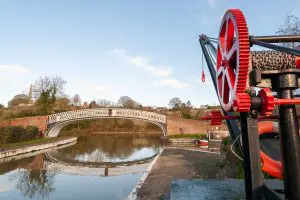 Horsley Iron Works cast-iron bridge at Braunston Marina, reflected in the canal beside a traditional red-and-black boatyard crane.