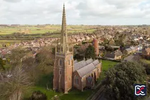 Aerial view of All Saints’ Church in Braunston with its prominent spire, surrounded by village homes and open Northamptonshire countryside.