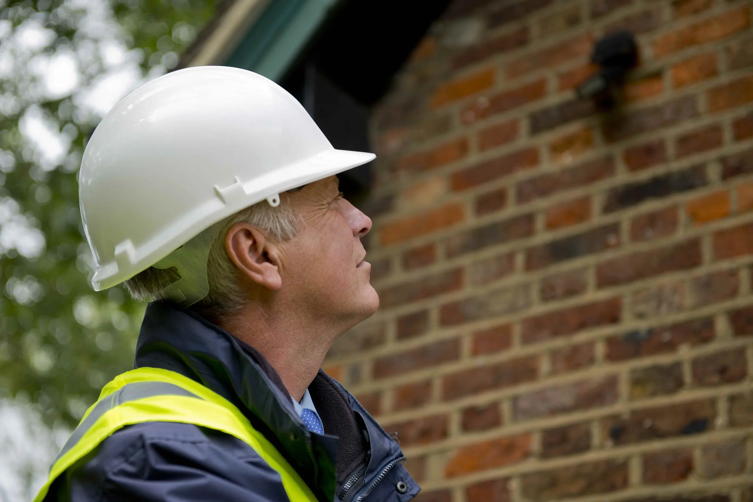 Surveyor examining external brickwork for cracks, damp or structural issues as part of a residential defect diagnosis inspection.