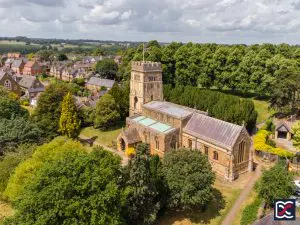 Aerial view of All Saints Church in Earls Barton, showing the distinctive Saxon tower surrounded by trees and village housing.