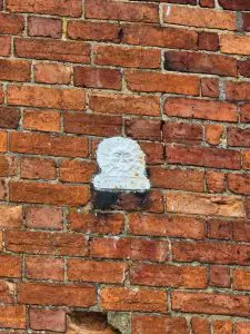 Overpainted Sun Fire Office fire mark plaque set into a brick wall, with the original sun motif faintly visible.