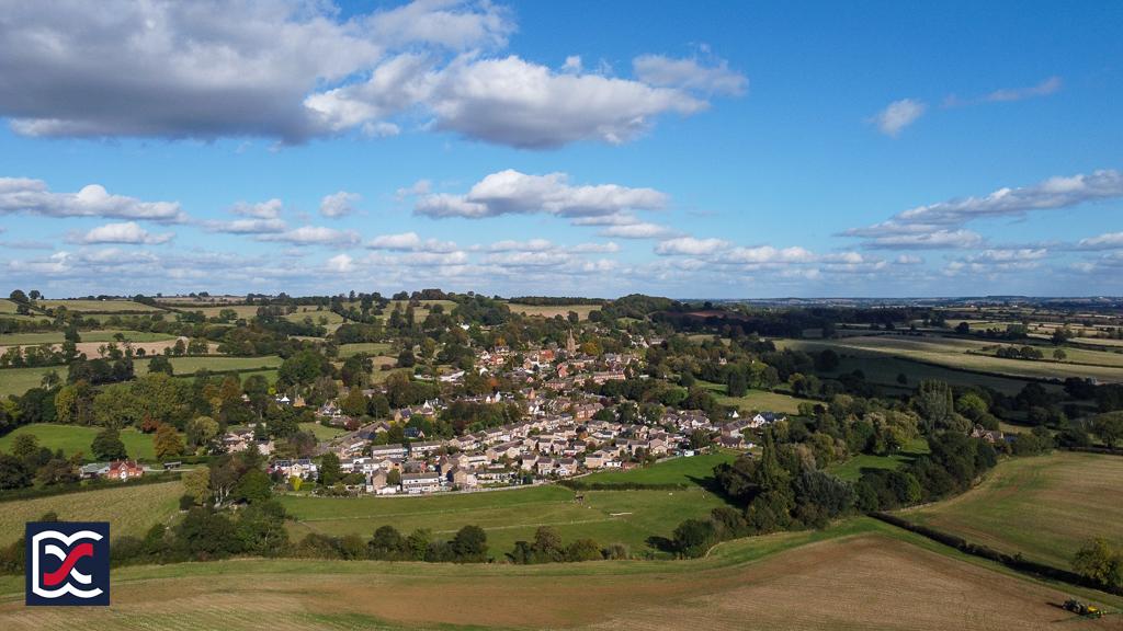 An aerial photograph of Newnham Village on sunny day with scattered white clouds. Taken from a high ridge near to Badby woods.
