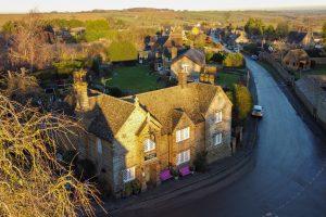 Aerial view of The King’s Arms public house in Farthingstone, surrounded by stone cottages and open Northamptonshire countryside.