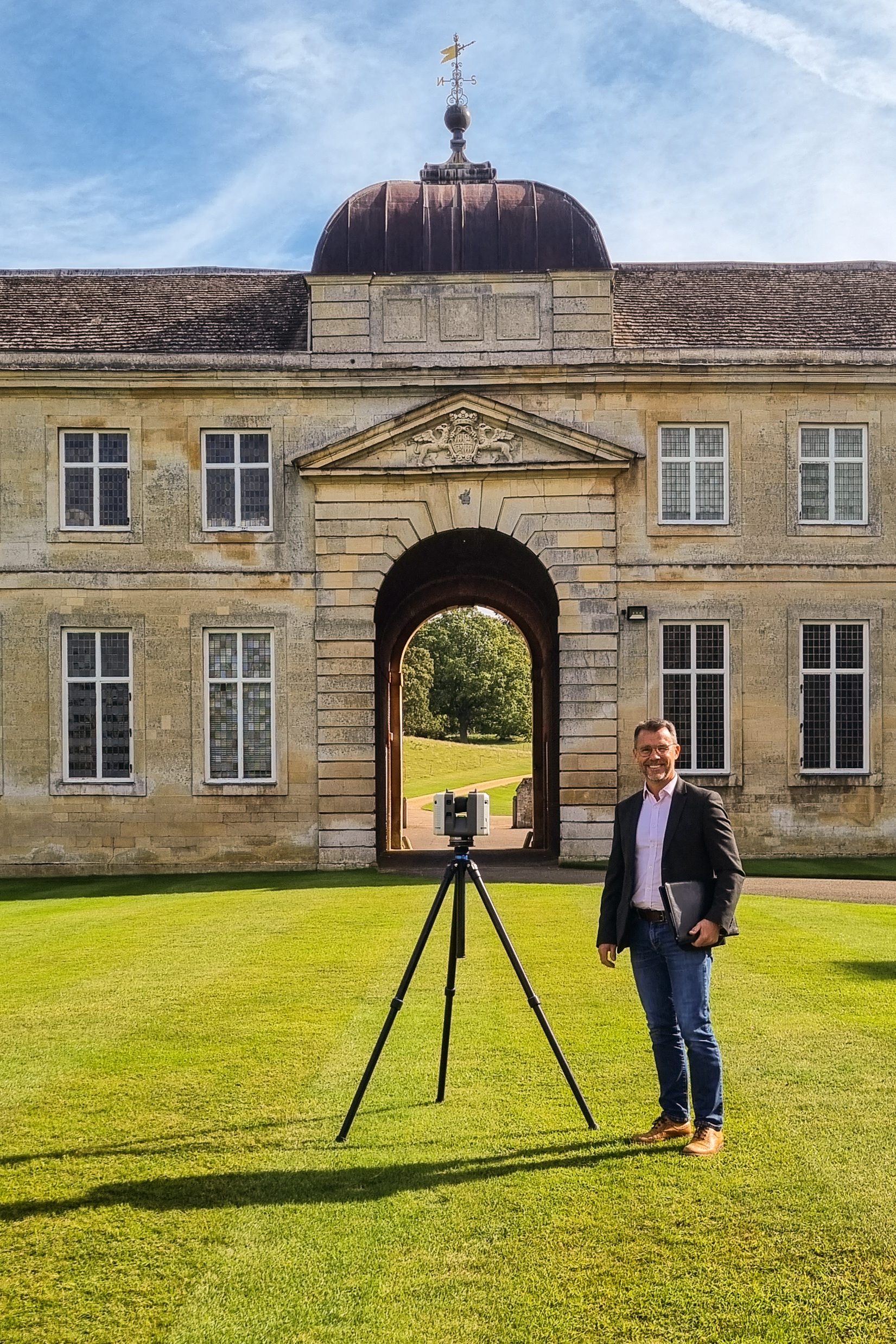 Chartered Surveyor carrying out a heritage measured building survey with a laser scanner in front of an historic stone gateway building.