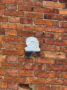 Overpainted Sun Fire Office fire mark plaque set into a brick wall, with the original sun motif faintly visible.